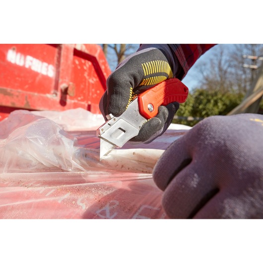 Photo of STANLEY 0-10-243 utility knife cutting plastic sheet outdoors, worker wearing gloves.