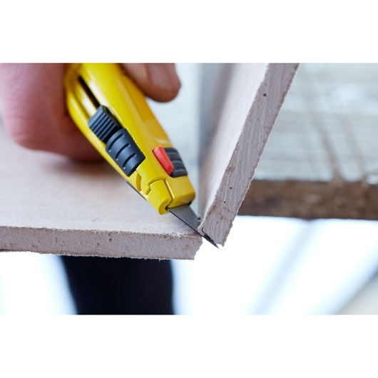 STANLEY 0-10-778 utility knife cutting drywall, close-up side angle.