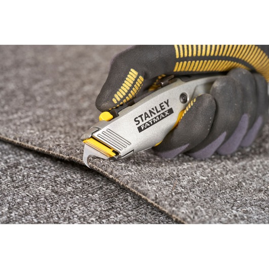STANLEY 0-10-789 utility knife cutting carpet, close-up, grey and yellow handle.
