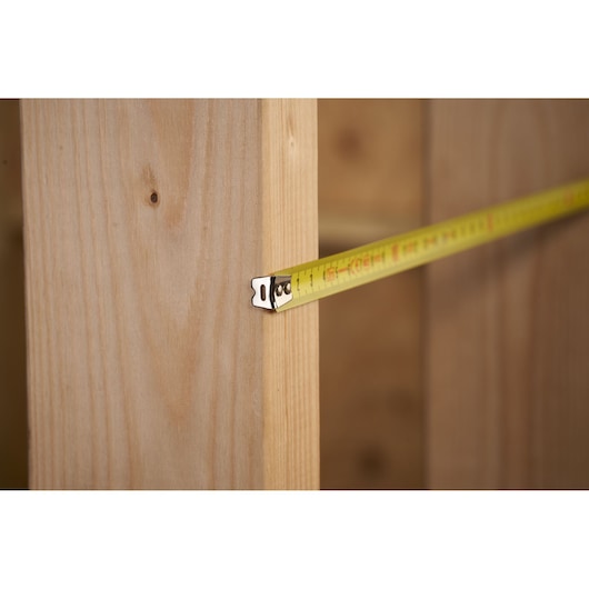 STANLEY 0-30-487 tape measure extended against wooden beam, side view, measuring distance.