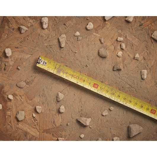STANLEY 0-30-497 tape measure on a dusty, wooden surface with scattered small rocks, shown from above.
