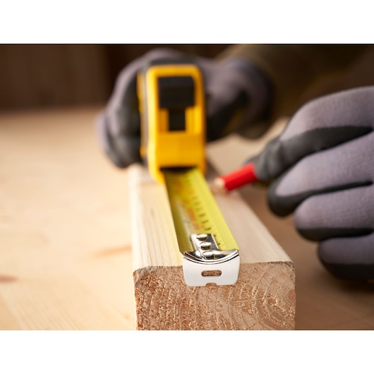 STANLEY 0-30-656 tape measure in use on wood, close-up photo shows yellow blade extended for measuring.