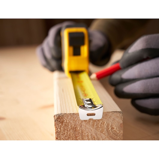 Photo of STANLEY 0-30-657 tape measure extended on wood, person marking with pencil, close-up view.