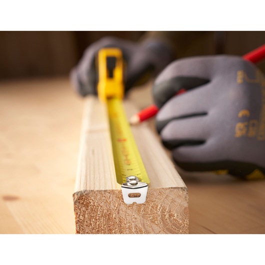 Photo of STANLEY 0-30-697 tape measure extended on wood with gloved hand marking measurement.