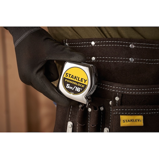 STANLEY 0-33-158 tape measure held by gloved hand, clipped to stitched brown tool belt.
