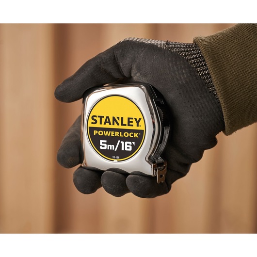 Photo of STANLEY 0-33-158 tape measure PowerLock held in gloved hand, showing 5m/16ft marking.