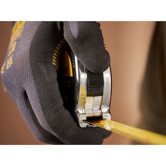 Photo of STANLEY 0-33-194 tape measure held in gloved hand, close-up view showing yellow measuring tape.