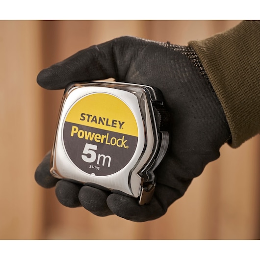 STANLEY 0-33-195 tape measure held in a gloved hand, PowerLock 5m, close-up photography.