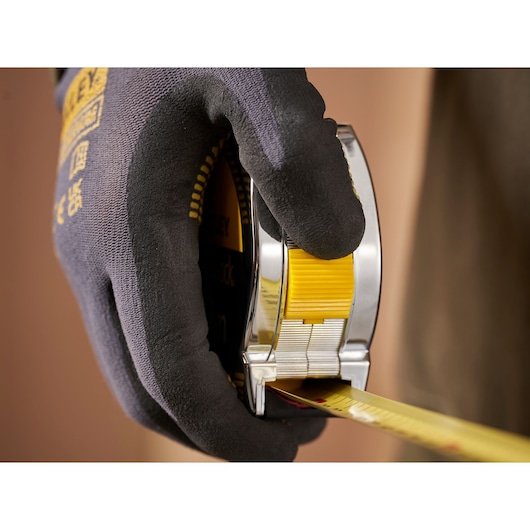 Photo of STANLEY 0-33-443 tape measure held in gloved hand, yellow and silver housing, close-up view.