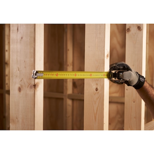 STANLEY 0-33-514 tape measure extended between wooden studs, close-up view, held by gloved hand.