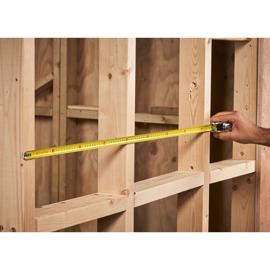 STANLEY 0-33-522 tape measure extended across wooden wall studs, product in use, close-up view.