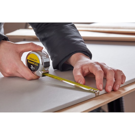 STANLEY 0-33-522 tape measure held by hand, measuring board surface, close-up photography.
