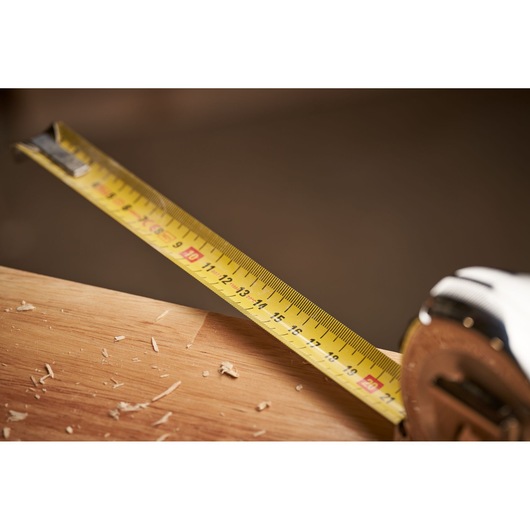 STANLEY 0-33-532 tape measure in use on wood, close-up side angle, yellow blade with black markings.