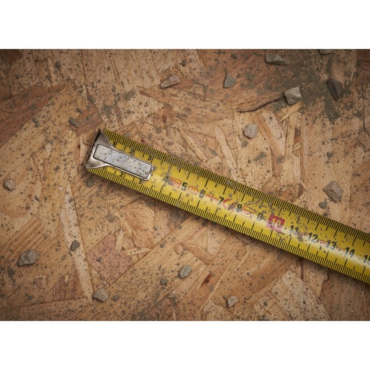 STANLEY 0-33-532 yellow tape measure on wood board with scattered stones, close-up view.