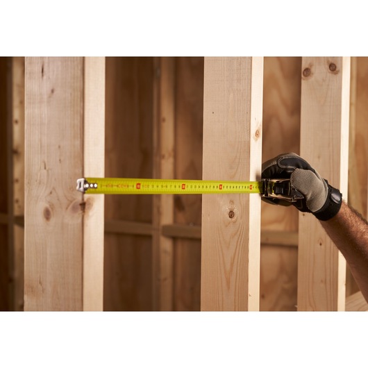 STANLEY 0-33-552 tape measure in use, measuring between wooden beams, held by gloved hand.