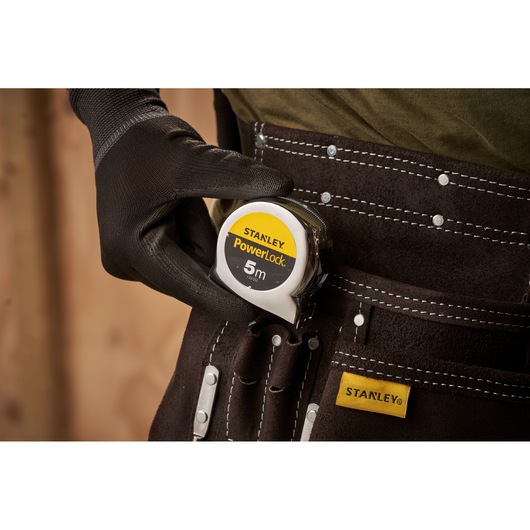 Photo of STANLEY 0-33-552 tape measure PowerLock 5m in a brown tool belt pocket with a gloved hand.