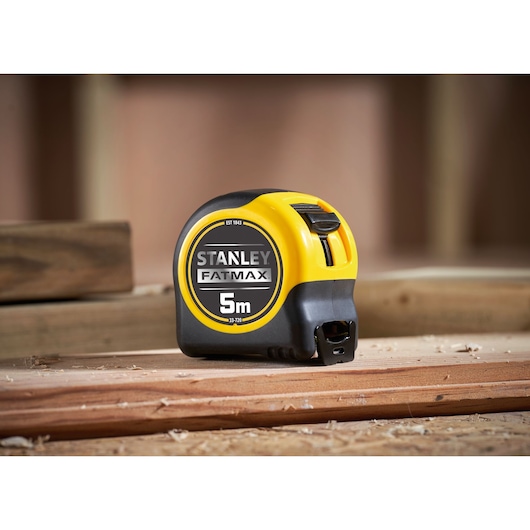 STANLEY 0-33-720 tape measure, 5m FatMax, black and yellow casing, on wooden boards, photography