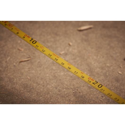 STANLEY 0-34-108 yellow tape measure with metric markings, close-up side view on sandy surface.