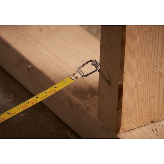 STANLEY 0-34-133 tape measure with yellow blade hooked on nail in wood frame, close-up photography.
