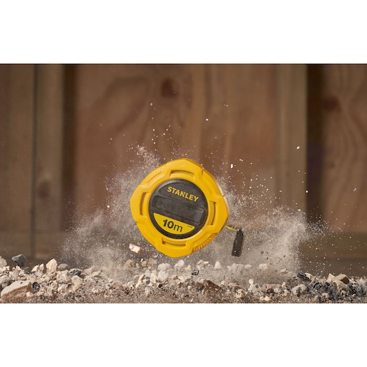Stanley 0-34-295 tape measure, yellow casing, 10m, shown on rocky ground with dust in the air.