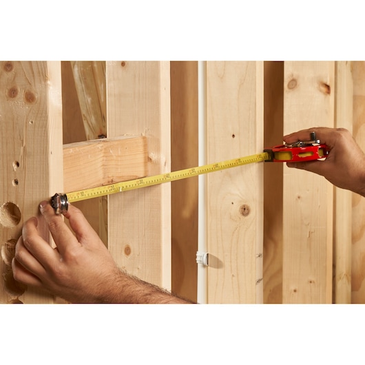 STANLEY 0-34-406 tape measure in use measuring wooden studs, close-up angle.