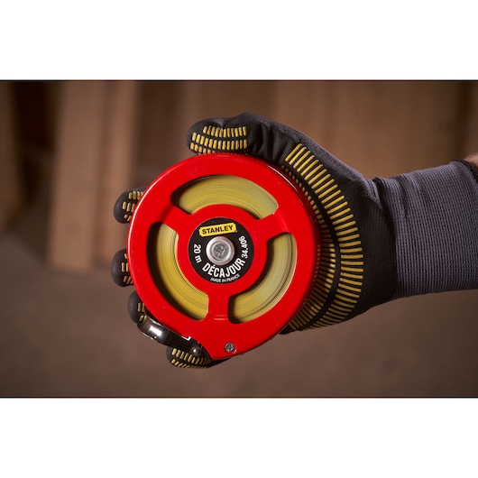 STANLEY 0-34-406 measuring tape with red case and yellow tape, held in a gloved hand, close-up view.