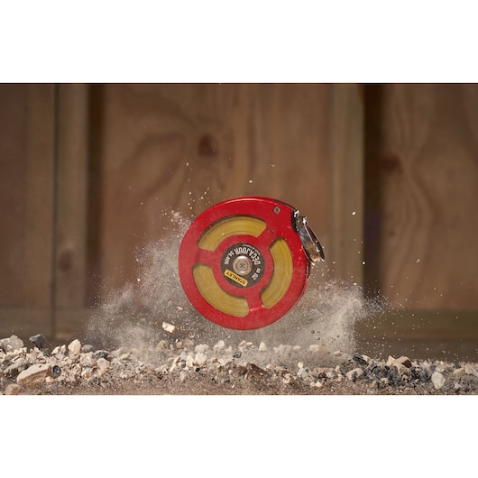 Stanley 0-34-406 red open reel measuring tape on rocky ground, construction setting.