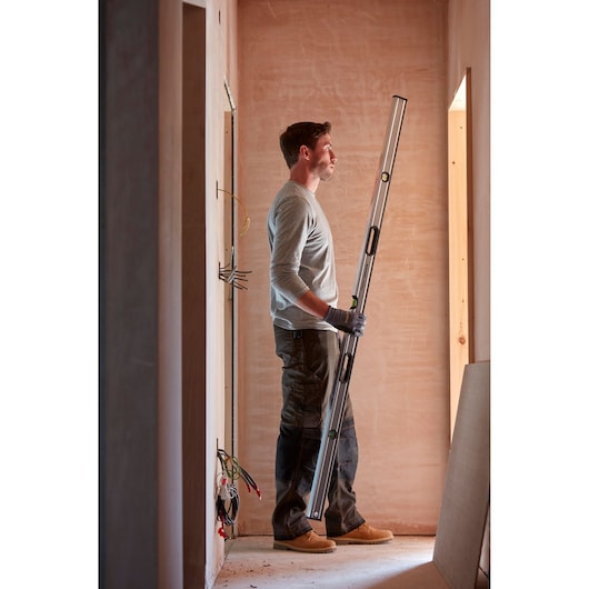 STANLEY 0-43-672 spirit level held by worker in unfinished room, vertical view, construction context.