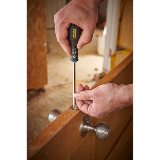 Photo of STANLEY 0-65-337 screwdriver in use tightening a door hinge screw, close-up context photography.