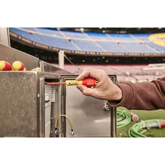 STANLEY 0-65-443 insulated screwdriver used at electrical box outdoors, red and yellow handle visible.