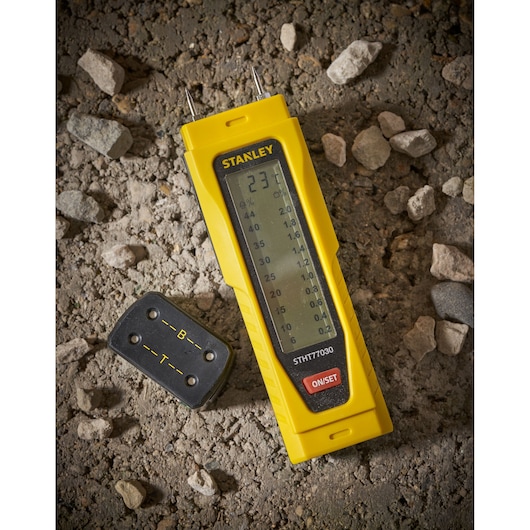 STANLEY 0-77-030 moisture meter with display and probe, angled view on rough ground.