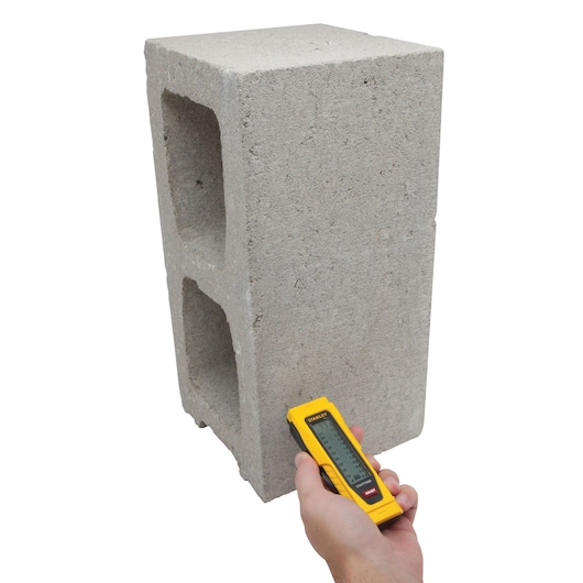 STANLEY 0-77-030 laser distance measurer applied to concrete block, front angle, product demonstration.