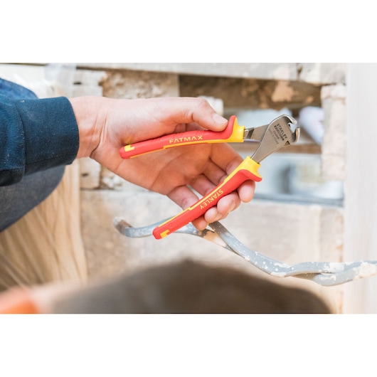 Photo of STANLEY 0-84-016 insulated pliers with red and yellow handles held by a hand, used on metal wire.