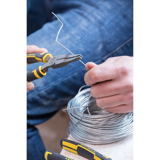 STANLEY 0-84-495 pliers in use, cutting silver wire, close-up, with coil and jeans visible.