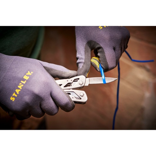 STANLEY 0-84-519 multitool blade cutting blue wire, close-up, worn with STANLEY gloves.