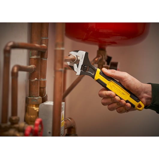 Stanley 0-90-947 adjustable wrench with yellow and black handle used on copper pipes, side angle.