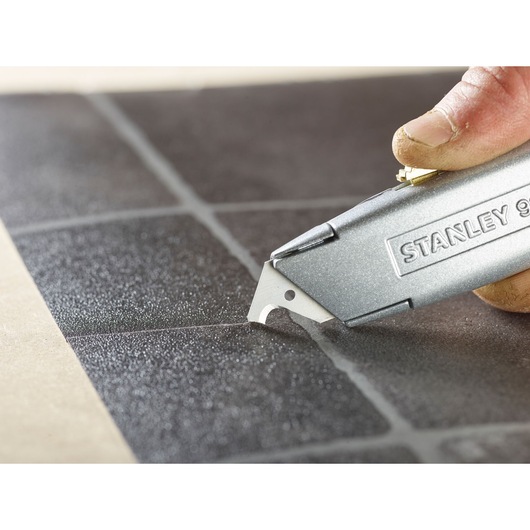 Photo of STANLEY 1-11-802 utility knife cutting black tile grout line, close-up angle.