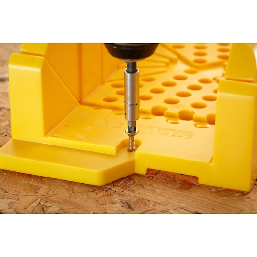 STANLEY 1-20-600 yellow plastic mitre box with drill in action, front angle, on wooden surface.