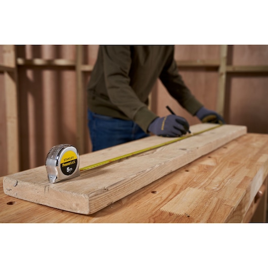 STANLEY 1-33-522 tape measure on wood plank, person measuring for carpentry.