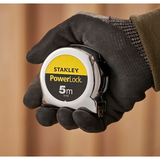 STANLEY 1-33-552 PowerLock 5m tape measure held in a gloved hand, close-up photography.