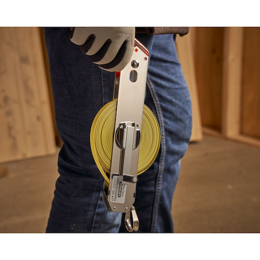 STANLEY 1-34-477 open reel tape measure with yellow blade, held by a gloved hand at a construction site.