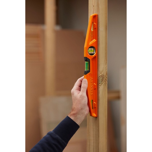 STANLEY 1-42-312 orange spirit level held vertically against wooden beam, photography.