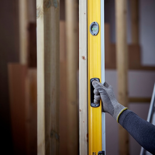 STANLEY 1-43-572 spirit level in use, yellow body with hand in work glove holding handle, construction background.