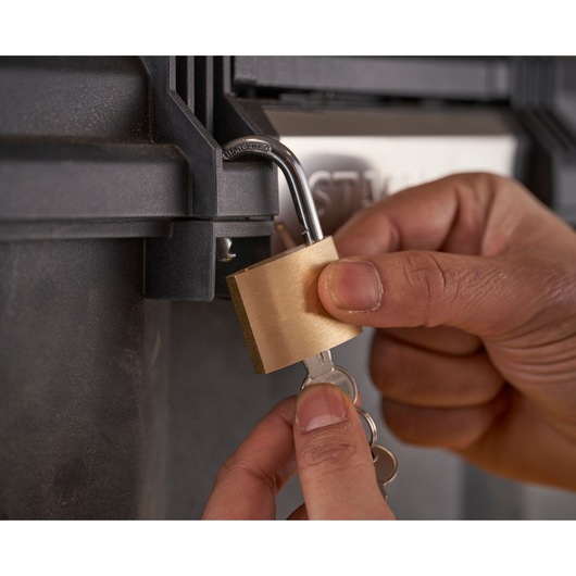 STANLEY 1-79-206 brass padlock being unlocked by hand on black storage box, close-up photography.