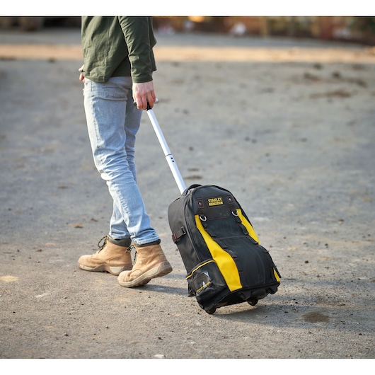 Photo of STANLEY 1-79-215 rolling tool bag with yellow and black design, extended handle, outdoors on gravel.