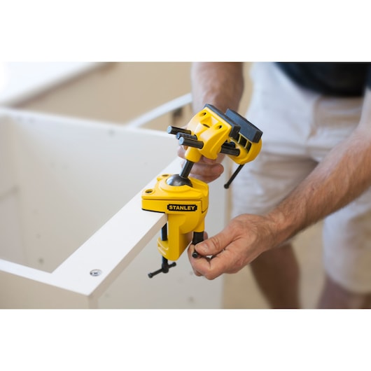 STANLEY 1-83-069 yellow swivel clamp holding a workpiece, shown in use by hand.