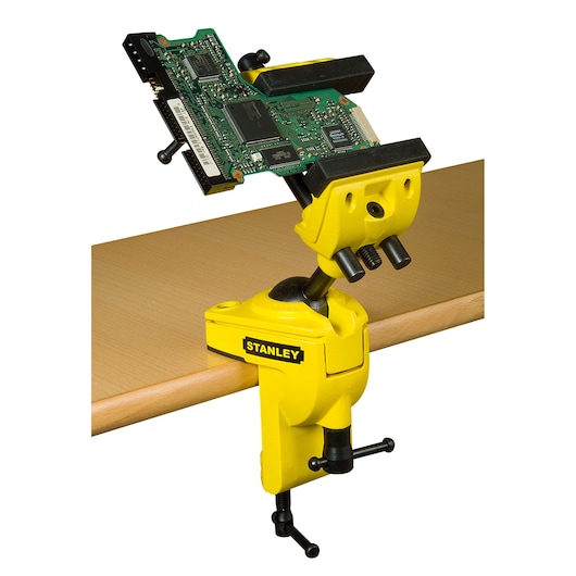 STANLEY 1-83-069 bench vise with yellow body and adjustable jaw, clamped to table holding circuit board, side view.