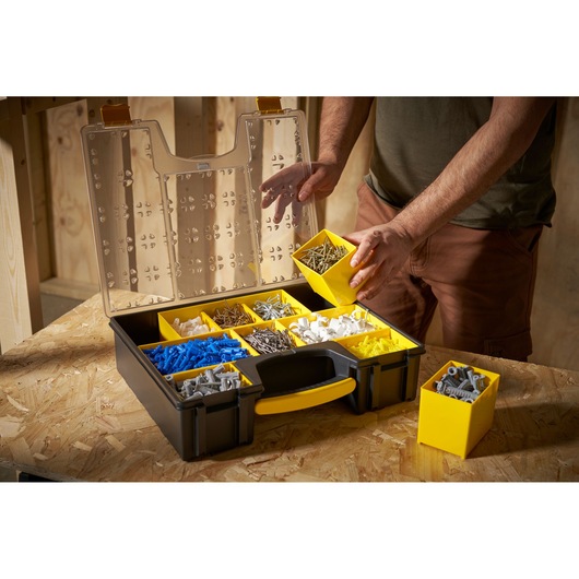 STANLEY 1-92-749 organizer box with yellow removable compartments, filled with assorted screws and wall plugs, on a workbench.
