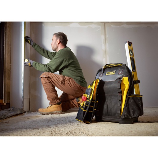 STANLEY 1-95-611 tool backpack with tools and level, shown upright on floor at construction site.