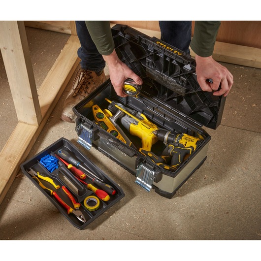 STANLEY 1-95-618 toolbox with open lid, filled with tools including drills, tape measure, level and hand tools on floor.